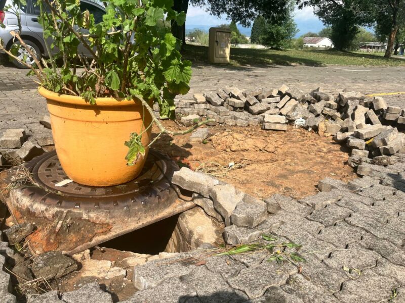 Damaged pavement and exposed drain covered with a plant pot.