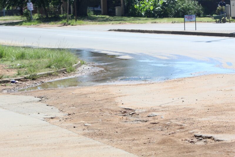 A massive sewage spill photographed on a suburban road with shops and homes in the background.