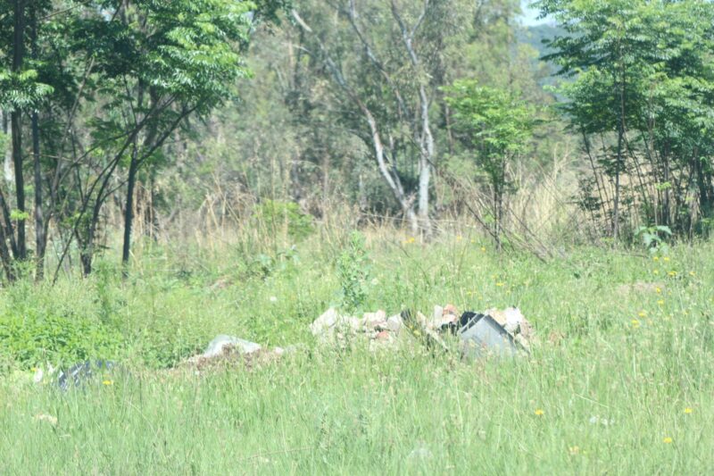 Illegal dumping of building rubble and household refuse is pictured in an open field.
