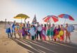 Image of group of people with colourful umbrellas on the beach, some are holding plastic balls and others are holding cut out waves.