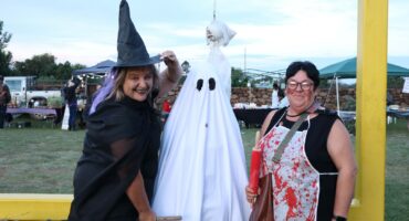 Two women dressed in Halloween costumes, one as a witch and the second woman with a bloody butcher apron on, posing with a ghost decoration at an outdoor Halloween event in Newcastle KwaZulu-Natal.