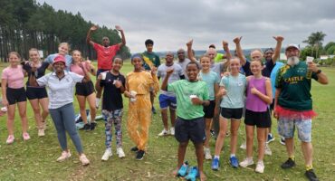 Runners of all ages in colourful running attire waves with hands in the air.
