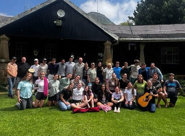 Image of group of Afrikaans male and female high school learners in front of a building sitting and standing on green grass while smiling at the camera.
