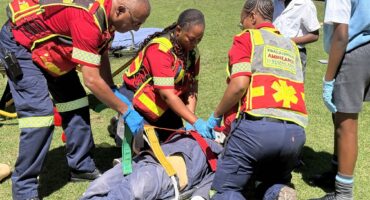 Image of three emergency personnel strapping a dummy to an emergency plank while learners are watching.