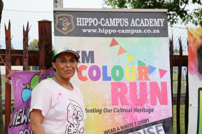 A woman stands smiling beside a Hippo-Campus Academy Colour Run poster at the event venue.
