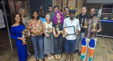 Group of atheles dressed in Disco attire at the prize giving, holding their trophies.