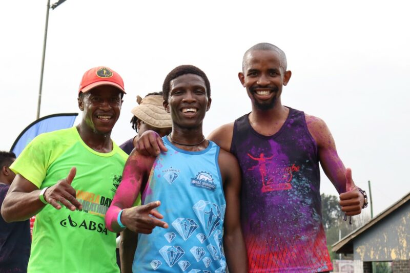 Three smiling participants pose after completing the Hippo-Campus Academy Colour Run, their shirts covered in bright colour powder.