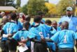 A man is coaching a young rugby team. Uniform is blue and the coach is wearing a blue and white cap.