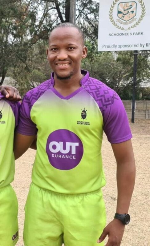 A photo of a young man dressed in Outsurance sponsored referee attire outside on a field.
