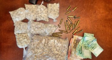 A revolver, several bags of mandrax drugs, scattered bullet casings, and stacks of assorted money notes are displayed on a wooden table after being seized by the Madadeni Police during a stop-a-search-operation.
