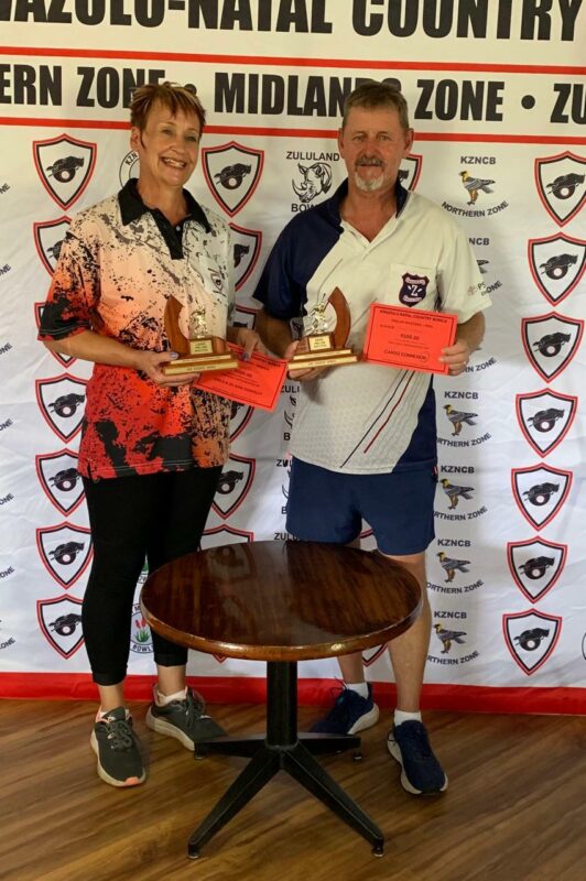 Two bowlers (one man and one woman) pose in front of a Kwazulu-Natal Country Bowls banner.