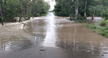 The Amcor Dam in Newcastle is pictired overflowing and flooding the road, which was forced to close as a result. Blockades are seen in the background behind the dam water.