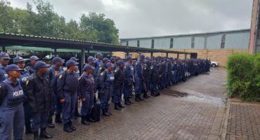 Dozens of police officers stand on parade in front of the Amajuba District SAPS office building.