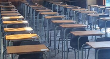 Image of the sun shining through an exam hall with desks and chairs.