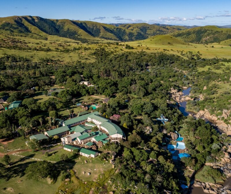 An image capturing a drone view of Gooderson Natal Spa Hot Springs and Leisure Resort, surrounded by trees, greenery and swimming pools.