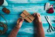 Woman is wrapping christmas presents on blue wooden table.