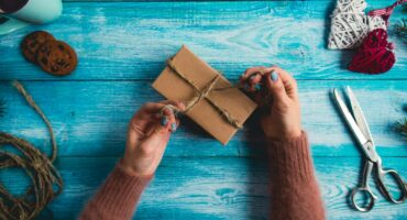 Woman is wrapping christmas presents on blue wooden table.