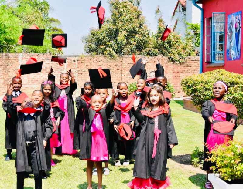 A group photo of Wonderland Pre-Primary School's Graduating class. Children are dressed in their black and red graduation gowns throwing caps in the air.