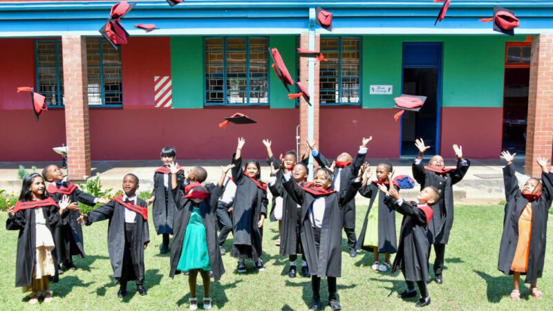 A group photo of Wonderland Pre-Primary School's Graduating class. Children are dressed in their black and red graduation gowns throwing caps in the air.