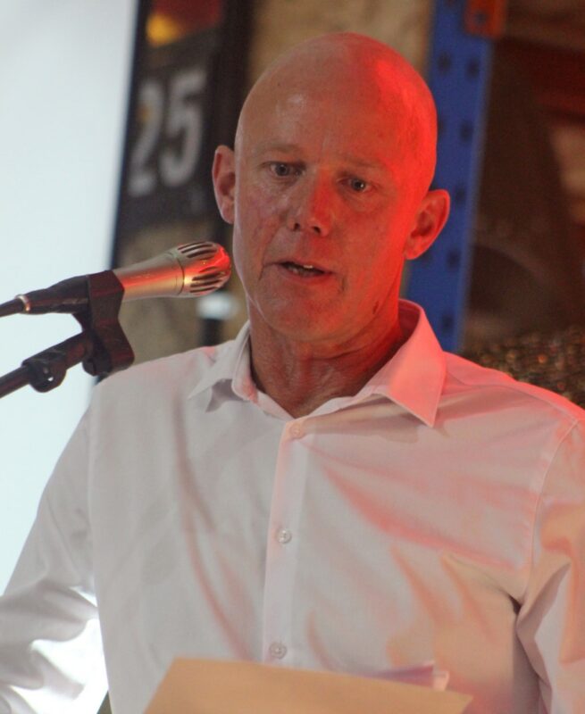 A bald male is photographed giving a speech during the 25 year celebration gala evening.