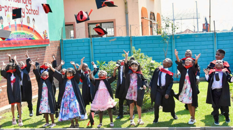 A group photo of Wonderland Pre-Primary School's Graduating class. Children are dressed in their black and red graduation gowns throwing caps in the air.