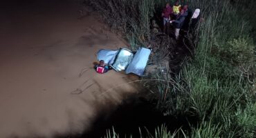 Image of part of a vehicle's roof sticking out murky water while divers are next to it.