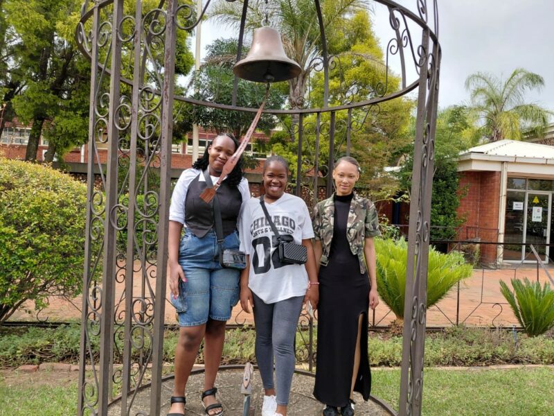 A photo showing learners from the Bridging Group 2025 taking turns to ring a ceremonial bell outdoors at Tugela Pre-Vocational School. Each photo features one or a small group of learners standing beneath the metal bell structure in a garden area with trees and school buildings in the background.