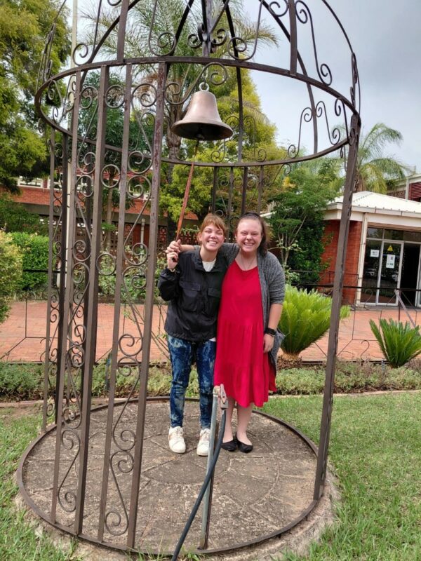 A photo showing learners from the Bridging Group 2025 taking turns to ring a ceremonial bell outdoors at Tugela Pre-Vocational School. Each photo features one or a small group of learners standing beneath the metal bell structure in a garden area with trees and school buildings in the background.