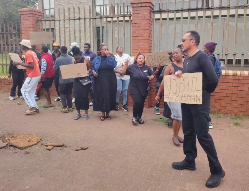 A large group of people gather outside of the Newcastle District Court holding placards opposing bail.