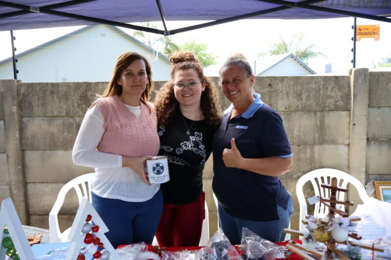 Three women stand behind a Christmas craft stall, smiling under a canopy.