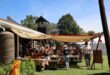 People browse stalls under shade canopies at an outdoor Christmas market beside a church building.