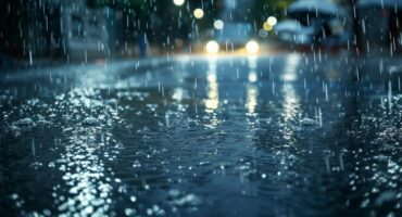 Image of rain falling in the dark in the street with car lights in the background.