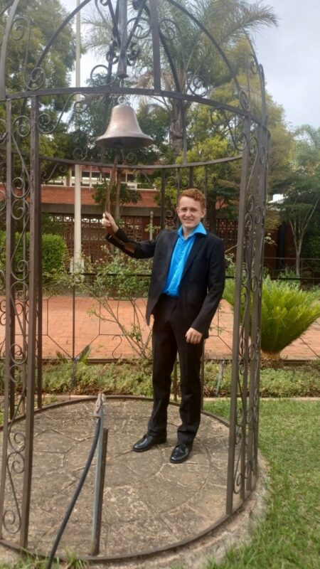 A photo showing learners from the Bridging Group 2025 taking turns to ring a ceremonial bell outdoors at Tugela Pre-Vocational School. Each photo features one or a small group of learners standing beneath the metal bell structure in a garden area with trees and school buildings in the background.