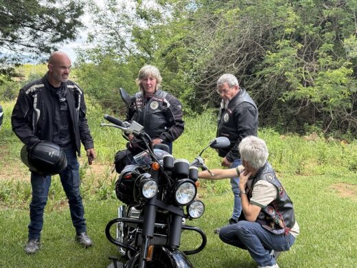 Image of bikers standing at a motorcycle dressed in black leather while talking.