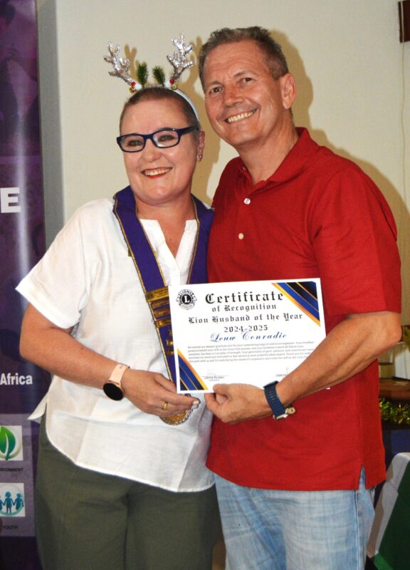 Two people (one woman and one man) posing in front of a Lions international Banner holding a certificate.