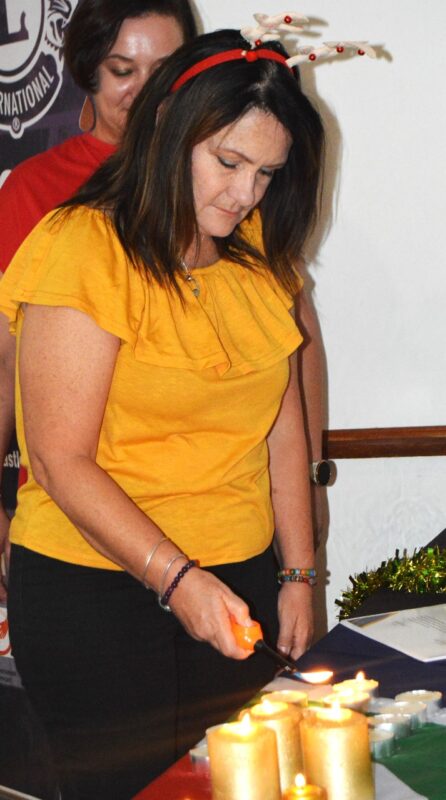 one woman wearing yellow is pictured lighting a candle during a ceremony.