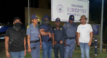 Several police officers stand in front of the Newcastle Police Station in their uniforms at night.