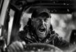 A black and white photo of an aggressive driver behind the steering wheel of his car.