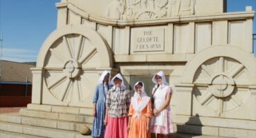 Image of traditionally Boer women in front of the concrete ox wagon at Blood River.