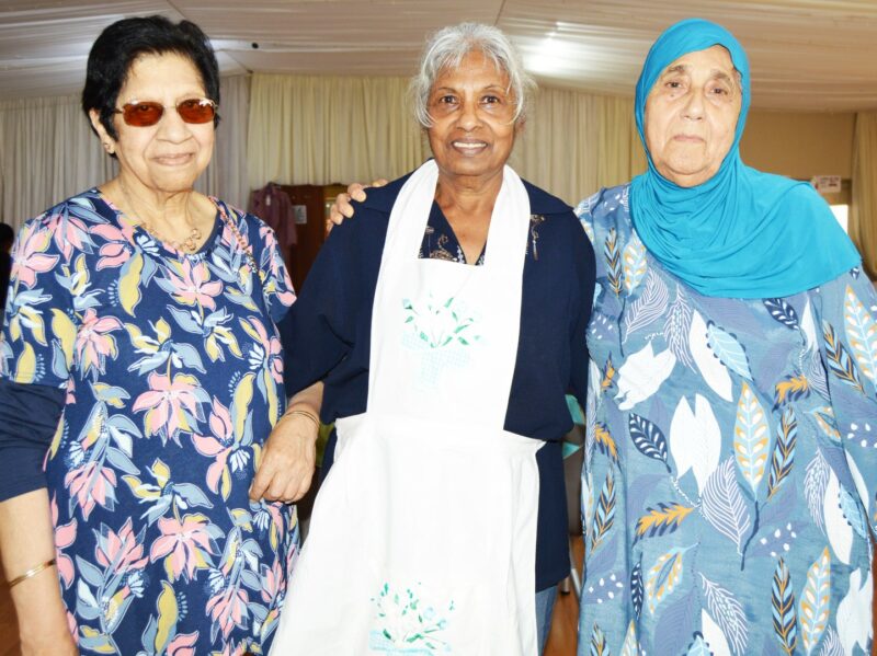 Three people appearing to be very excited pose for a picture during a Christmas Bazaar.
