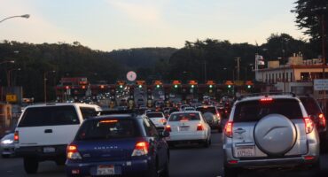 A toll road on a busy highway with dozens of vehicles passing through it.