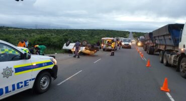 Image of an accident scene with bakkie rolled over, police and emergency services are on scene with orange cones directing other motorists.