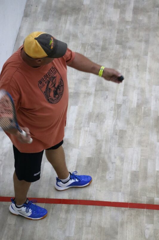 Squash player strikes ball during singles league match.