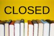 Books lined up on a shelf beneath the word closed on a yellow background.