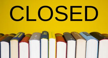 Books lined up on a shelf beneath the word closed on a yellow background.