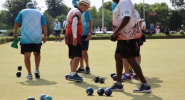 Bowls players gather on a green during a quadrangular tournament.