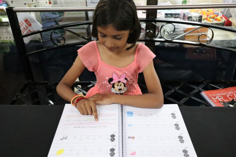Child practises writing letters in a children’s literacy workbook.