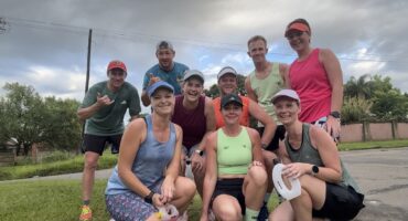 Image of group of men and women dressed in running clothes, some standing, others are kneeling after a long run.