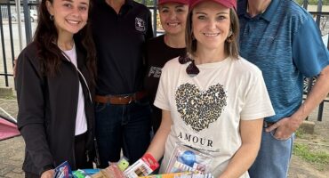 Image of women and a man standing under a Vryheid Athletic Club gazebo with a basket of stationery in front of them.