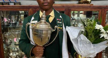 Image of young male learner with a trophy and flowers in his hands and 'crowned' as Dux learner of 2025 at Vryheid High School.